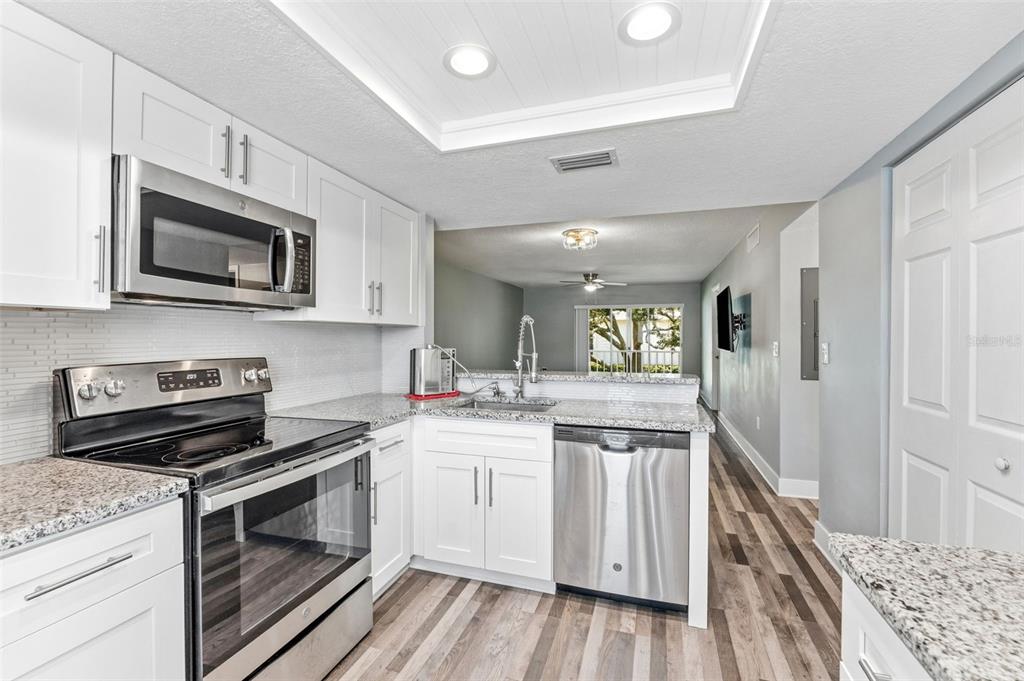 A modern kitchen features white cabinets, stainless steel appliances, granite countertops, and wood-look flooring — 126 CYPRESS COURT UNIT 26, OLDSMAR, FL