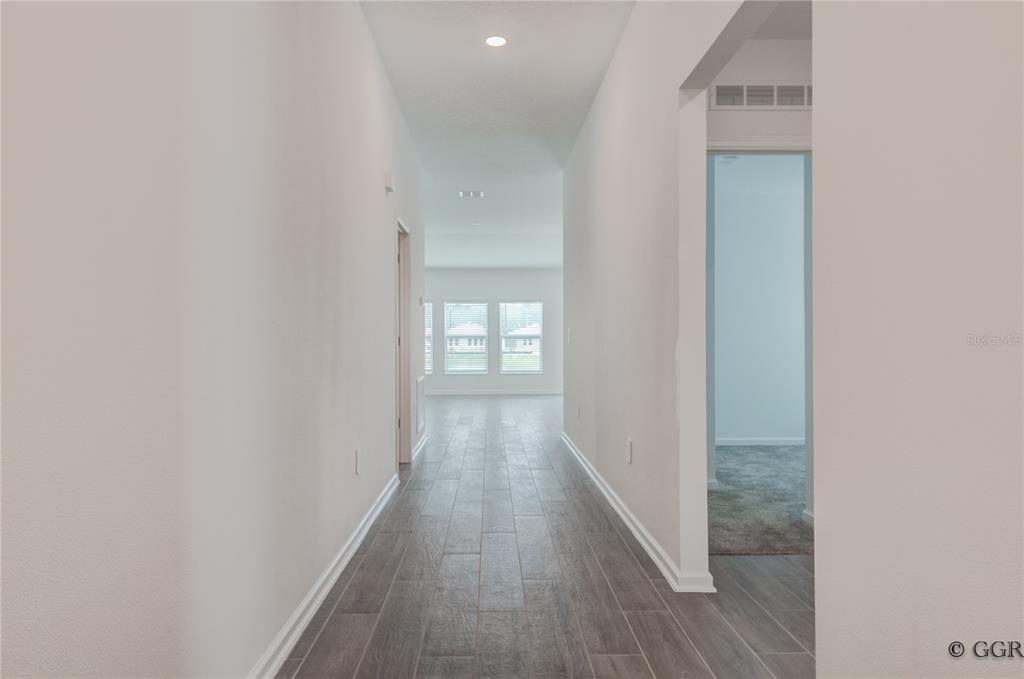 A hallway with wood-look tile flooring leads toward a room with large windows — 1490 BRENTWOOD DRIVE, KISSIMMEE, FL