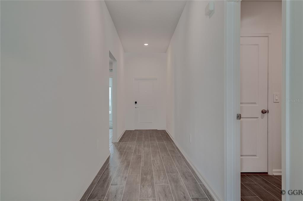 A hallway with white walls, a white door, and gray wood-look tile flooring — 1490 BRENTWOOD DRIVE, KISSIMMEE, FL