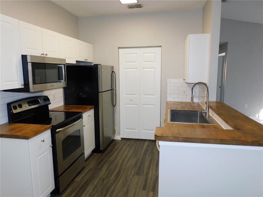 A kitchen features white cabinets, wood countertops, stainless steel appliances, and wood-look flooring — 844 GRAND REGENCY POINT UNIT 203, ALTAMONTE SPRINGS, FL