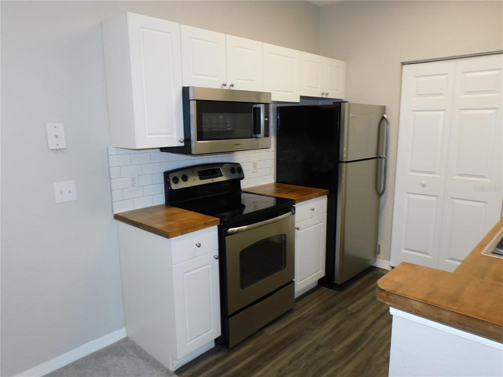 A kitchen features white cabinets, stainless steel appliances, a wood countertop, and a subway tile backsplash — 844 GRAND REGENCY POINT UNIT 203, ALTAMONTE SPRINGS, FL