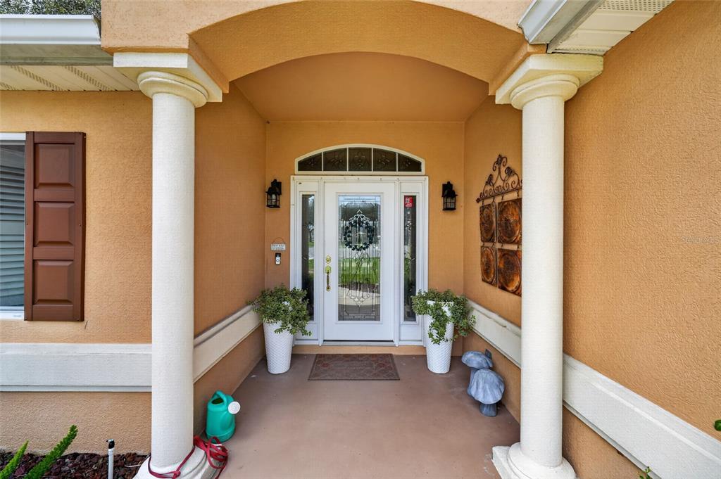 A covered front porch features two white columns, a glass-paneled front door, and potted plants — 13857 DEL WEBB BOULEVARD, SUMMERFIELD, FL