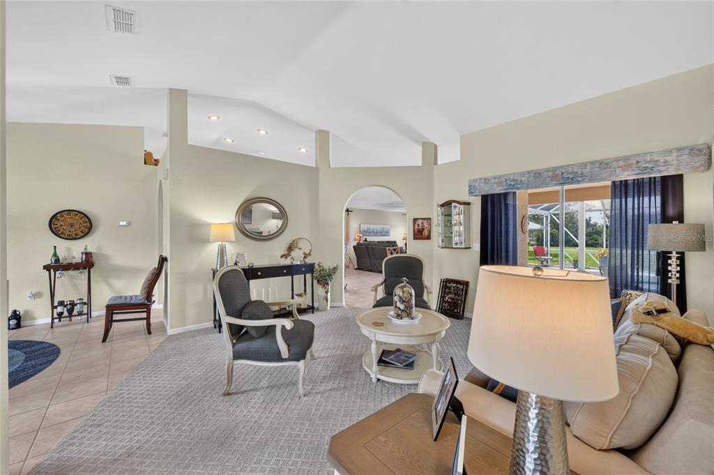 A living room with vaulted ceilings, carpeted flooring, and an arched doorway leading to another room — 13857 DEL WEBB BOULEVARD, SUMMERFIELD, FL