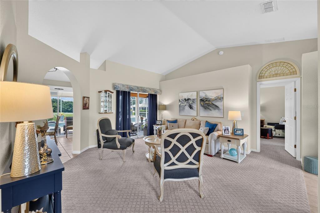 A living room features vaulted ceilings, carpeted floors, and a view of a pool area — 13857 DEL WEBB BOULEVARD, SUMMERFIELD, FL