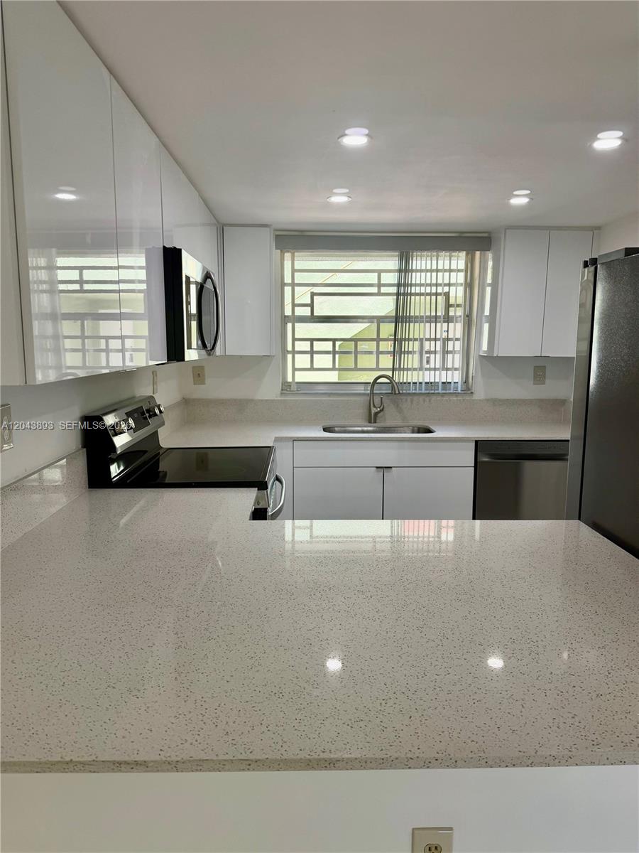 A modern kitchen features white cabinets, speckled quartz countertops, and stainless steel appliances — 11123 NW 7th St # 4, Miami FL 33172, MIAMI, FL