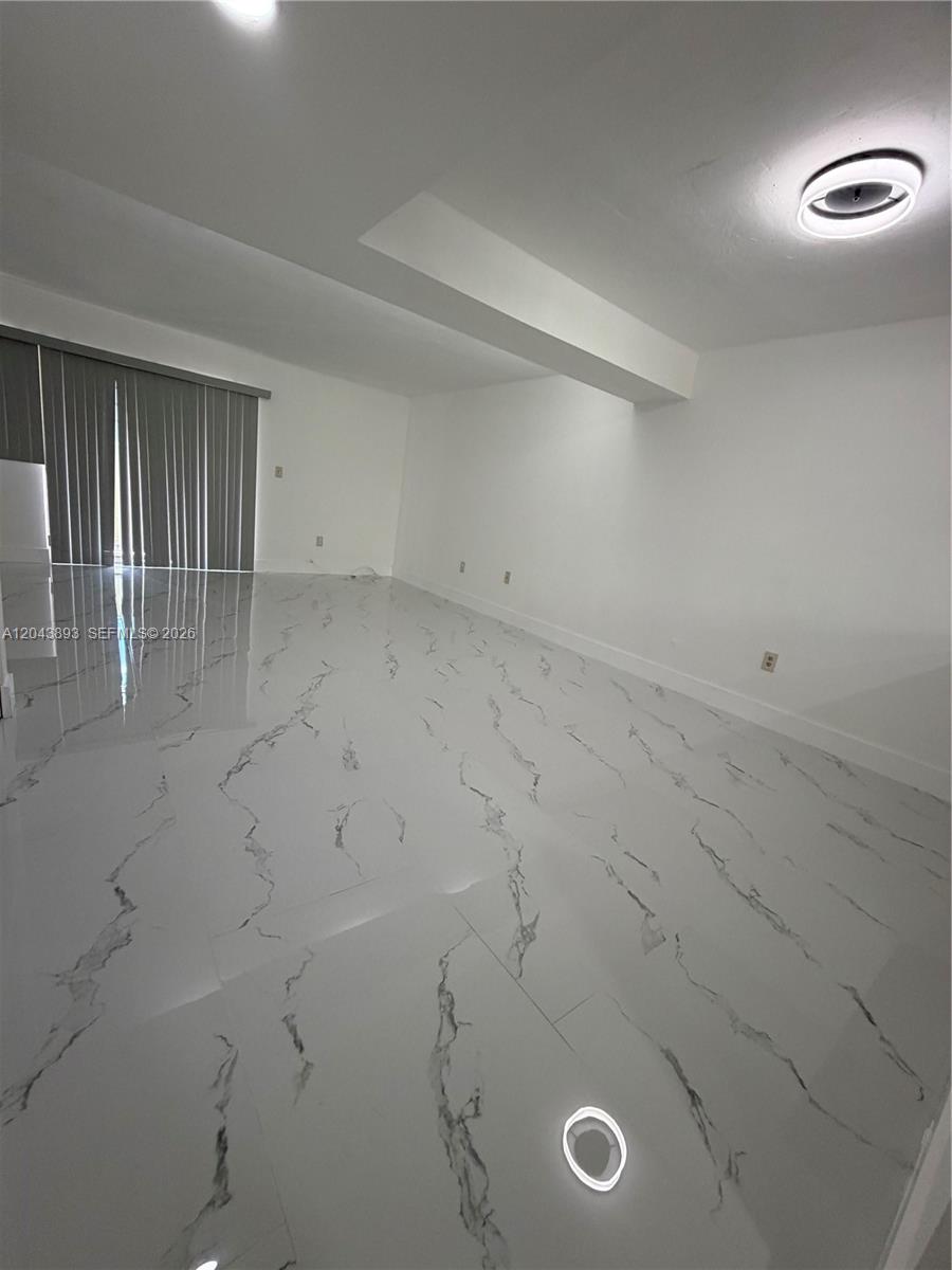 An empty room features white walls, a dropped ceiling beam, and white marble-patterned tile flooring — 11123 NW 7th St # 4, Miami FL 33172, MIAMI, FL