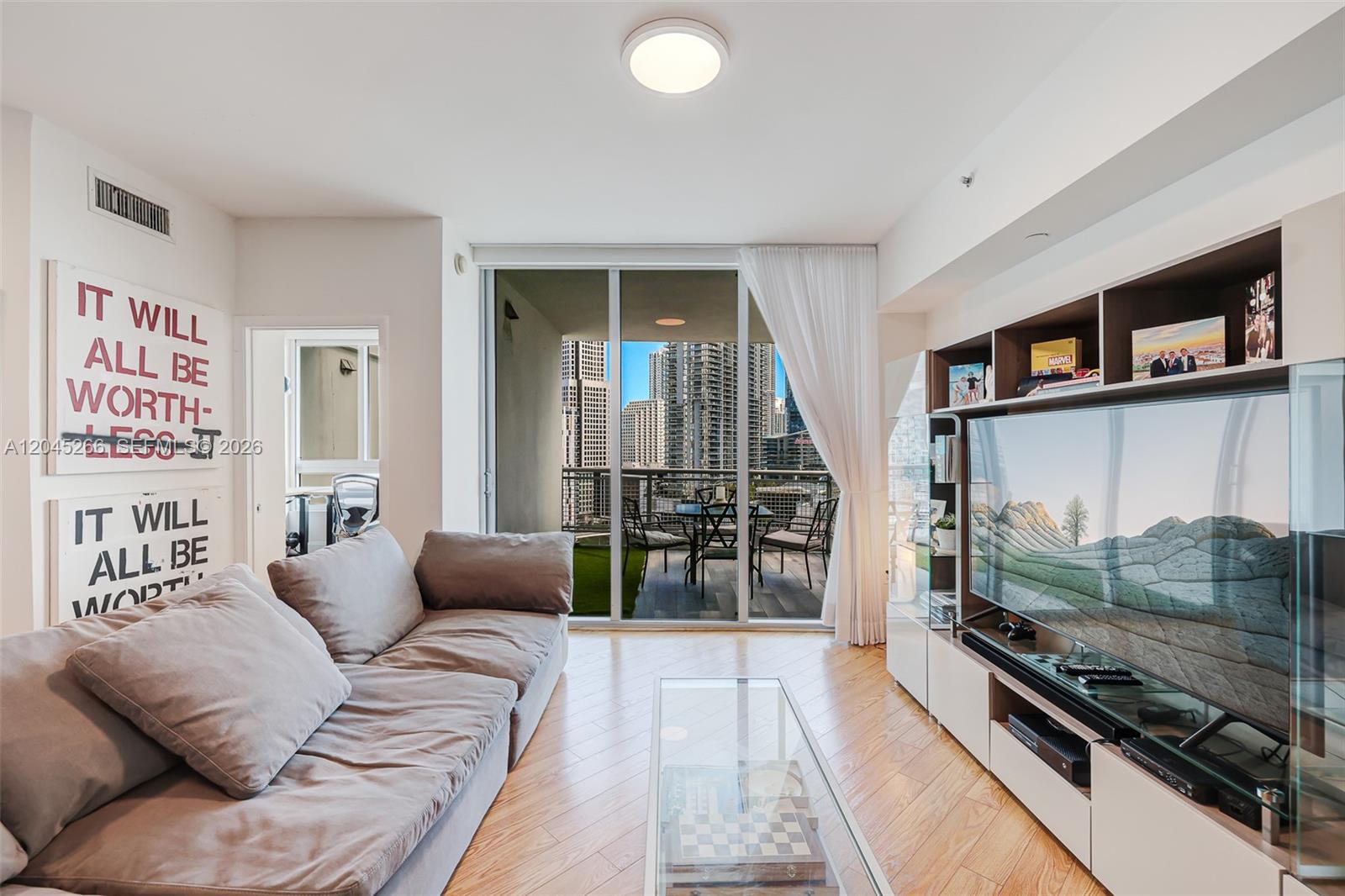 A modern living room features a grey sofa, glass coffee table, and a balcony view — 350 S Miami Ave # 2104, Miami FL 33130, MIAMI, FL