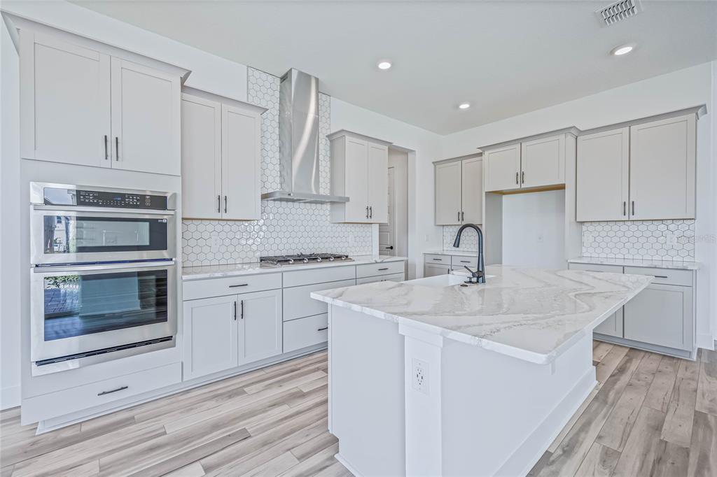 A modern kitchen features white cabinetry, a marble-topped island, stainless steel appliances, and hexagon backsplash — 17422 HONEYBELL TANGELO COURT, WINTER GARDEN, FL