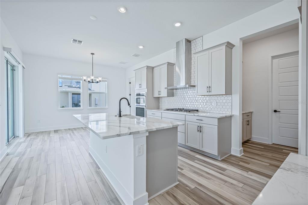 A modern kitchen features a marble-topped island, light gray cabinetry, and wood-look flooring — 17422 HONEYBELL TANGELO COURT, WINTER GARDEN, FL