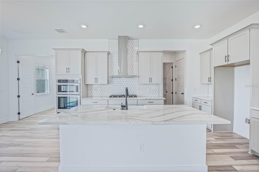 A modern kitchen features a white island, light gray cabinetry, and a white tile backsplash — 17422 HONEYBELL TANGELO COURT, WINTER GARDEN, FL