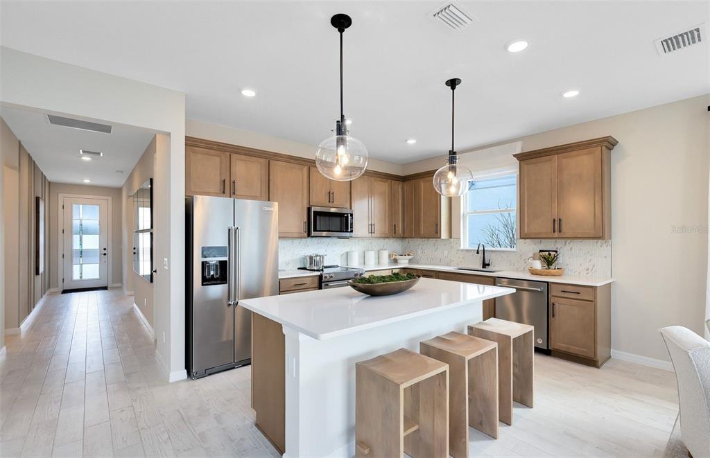 A modern kitchen features light wood cabinets, a white quartz island, and two glass pendant lights — 2132 BRANCHED OAK ROAD, ST CLOUD, FL