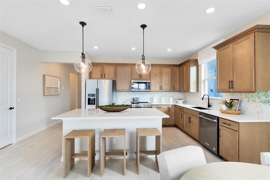 A kitchen features light wood cabinets, a white island with three stools, and stainless appliances — 2132 BRANCHED OAK ROAD, ST CLOUD, FL