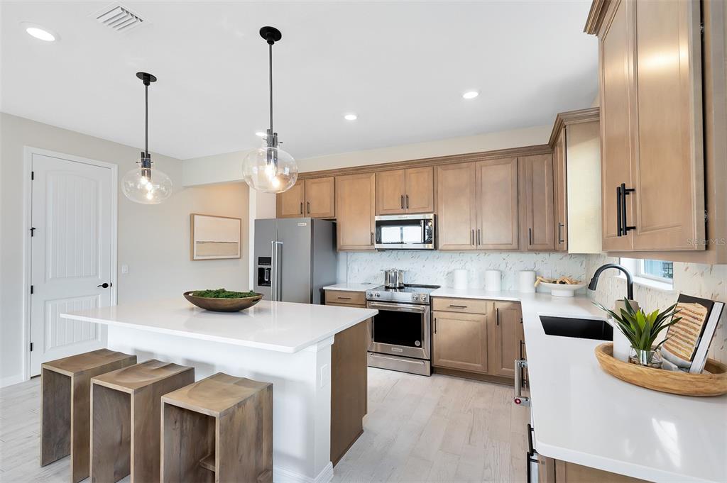 A modern kitchen features light wood cabinets, white countertops, a center island, and stainless appliances — 2132 BRANCHED OAK ROAD, ST CLOUD, FL