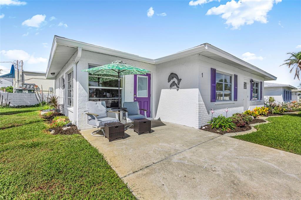 A white single-story house features a concrete patio with chairs, a green umbrella, and purple shutters — 1 PEARL STREET UNIT 1, ENGLEWOOD, FL