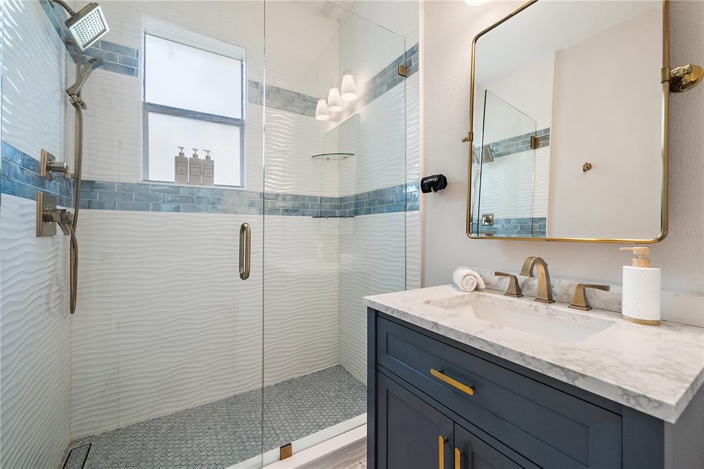 A modern bathroom features a glass-enclosed shower, a dark blue vanity, and gold-toned fixtures — 320 OHIO PLACE, SARASOTA, FL