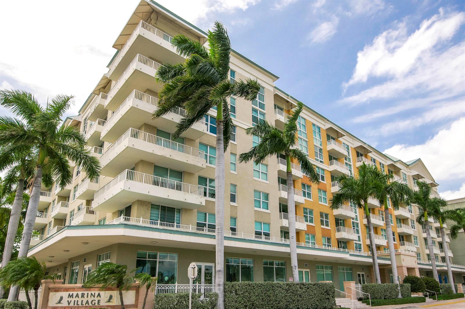 A multi-story apartment building with balconies and palm trees stands under a blue sky — 100 NE 6th Street # 407, Boynton Beach FL 33435, BOYNTON BEACH, FL
