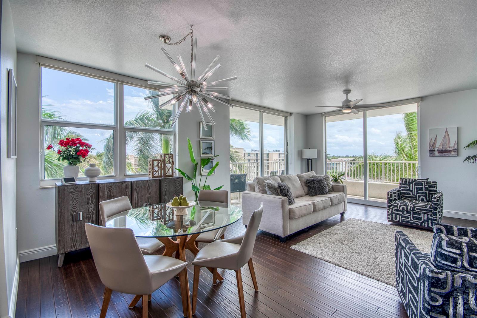 A bright living and dining area features dark wood floors, a glass table, and balcony views — 100 NE 6th Street # 407, Boynton Beach FL 33435, BOYNTON BEACH, FL