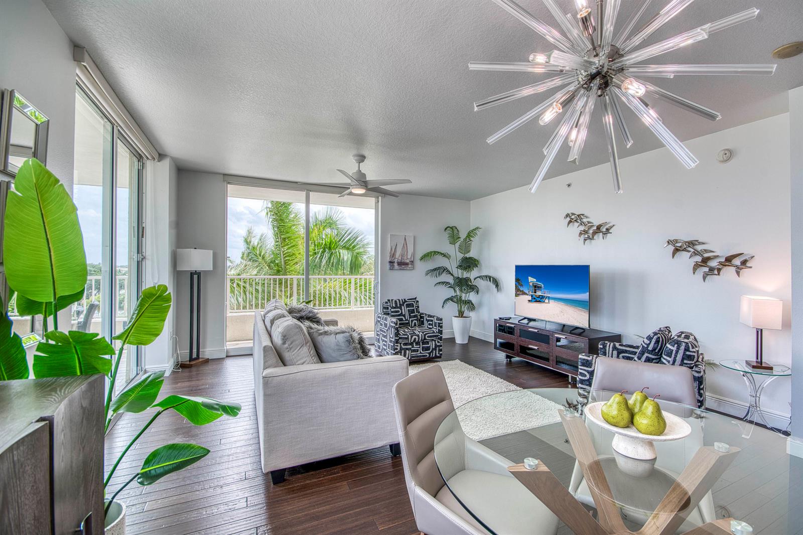 A living and dining room with a glass table, sofa, television, and balcony view — 100 NE 6th Street # 407, Boynton Beach FL 33435, BOYNTON BEACH, FL