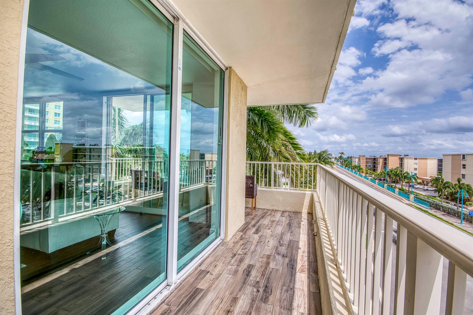 A balcony with wood-look tile flooring, white railings, and sliding glass doors overlooking a street — 100 NE 6th Street # 407, Boynton Beach FL 33435, BOYNTON BEACH, FL