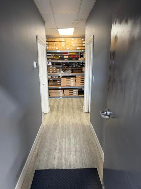 A hallway with gray walls and wood-look flooring leads to a room with storage shelving — 2560 N Powerline Road # 201, Pompano Beach FL 33060, POMPANO BEACH, FL