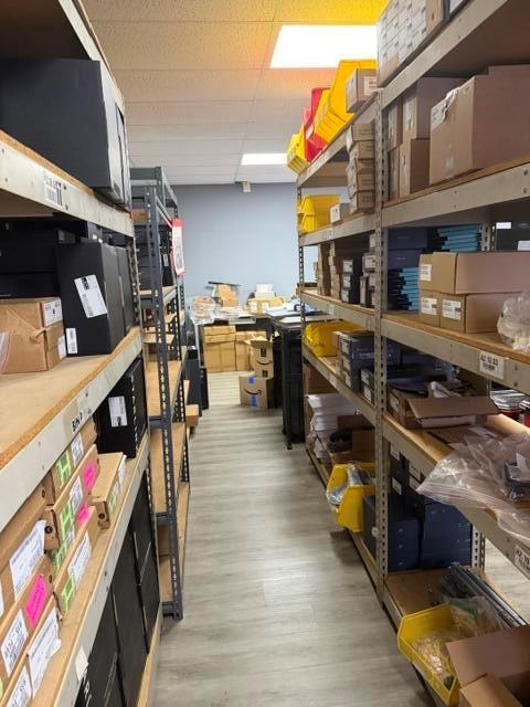 A narrow storage room features metal shelving units filled with various boxes and plastic bins — 2560 N Powerline Road # 201, Pompano Beach FL 33060, POMPANO BEACH, FL