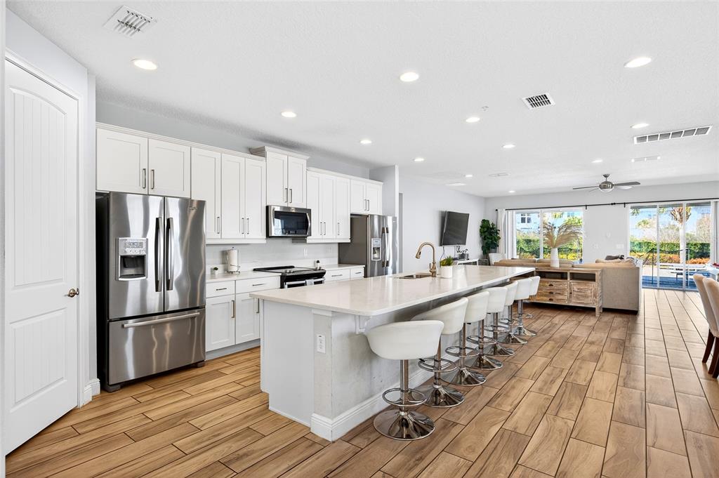 A modern kitchen features white cabinetry, stainless steel appliances, and a large island with seating — 7724 FAIRFAX DRIVE, KISSIMMEE, FL