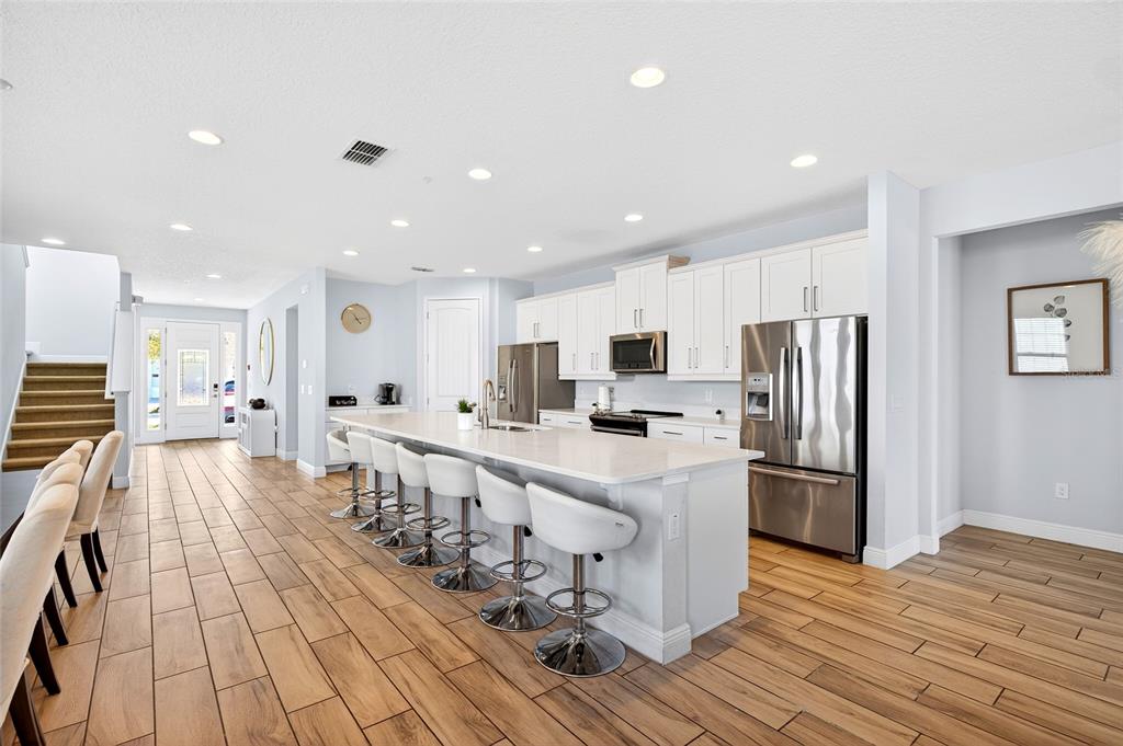 A modern kitchen features white cabinetry, a large island with bar seating, and wood-look flooring — 7724 FAIRFAX DRIVE, KISSIMMEE, FL