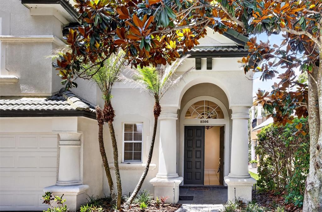 The exterior of a house features a dark front door, arched entryway, and palm trees — 8506 SAINT MARINO BOULEVARD, ORLANDO, FL