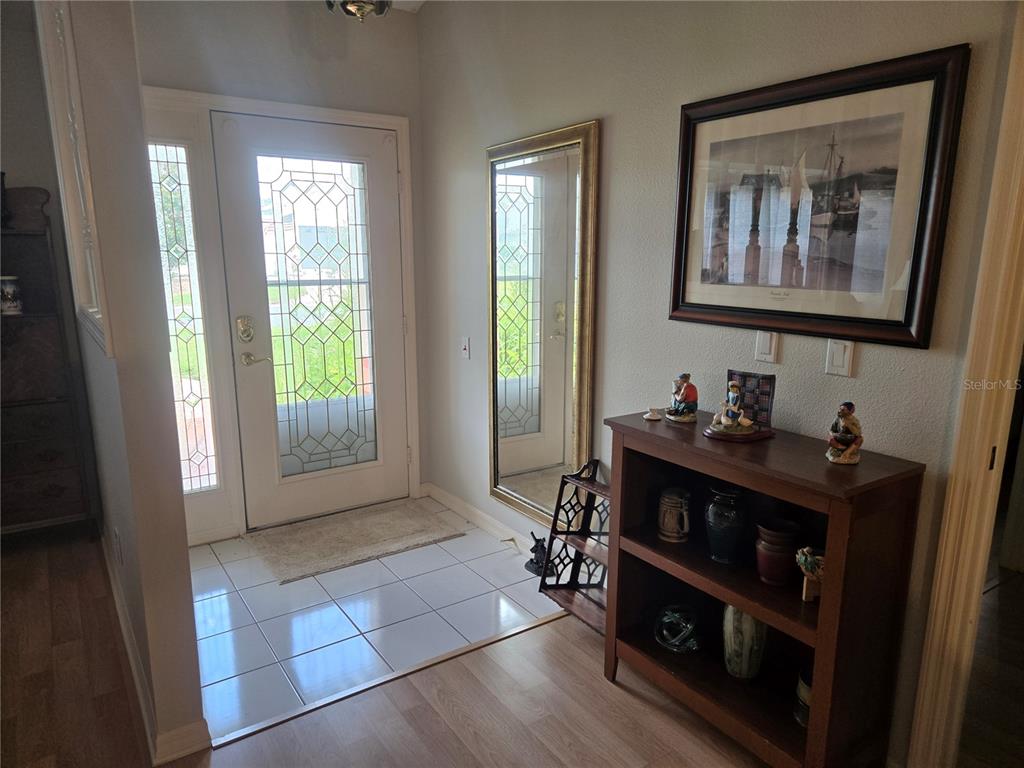 An entryway features a white front door with decorative glass, tile flooring, and a wooden bookshelf — 5506 PRINCE CHARLES LANE, LEESBURG, FL