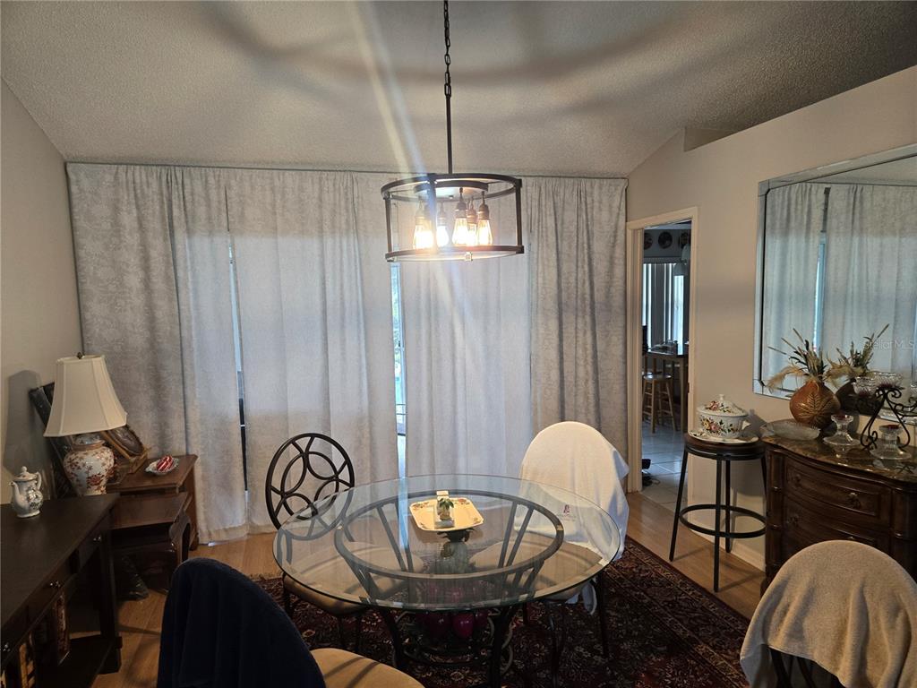 A dining room features a glass-topped table, a drum chandelier, and floor-to-ceiling curtains — 5506 PRINCE CHARLES LANE, LEESBURG, FL