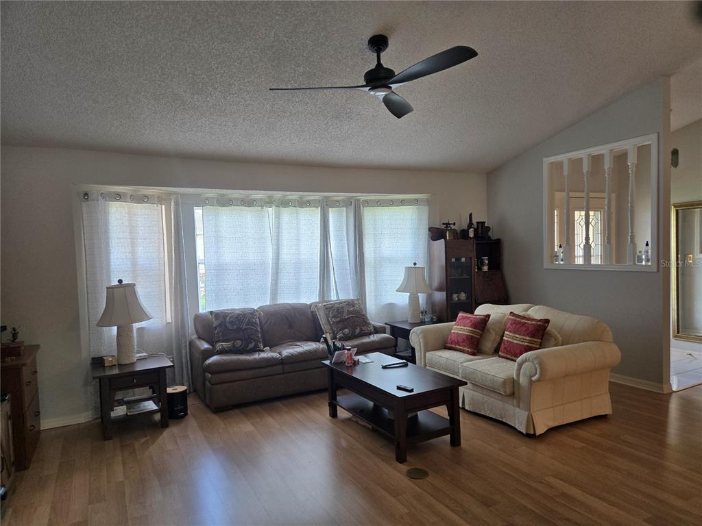 A living room features a ceiling fan, two sofas, a coffee table, and wood-look flooring — 5506 PRINCE CHARLES LANE, LEESBURG, FL