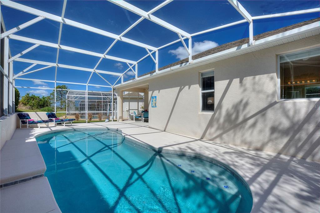 A swimming pool with a screen enclosure sits on a patio next to a house — 556 BONVILLE DRIVE, DAVENPORT, FL