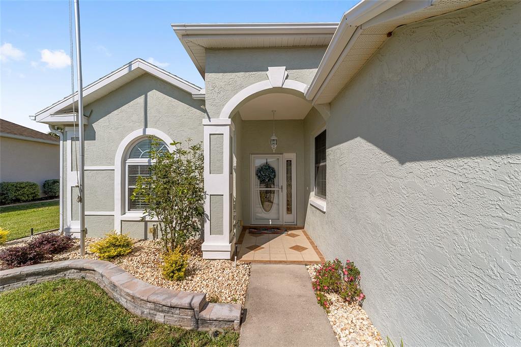 The exterior of a light green house features a covered entryway with a tiled floor — 5751 NW 25TH LOOP, OCALA, FL