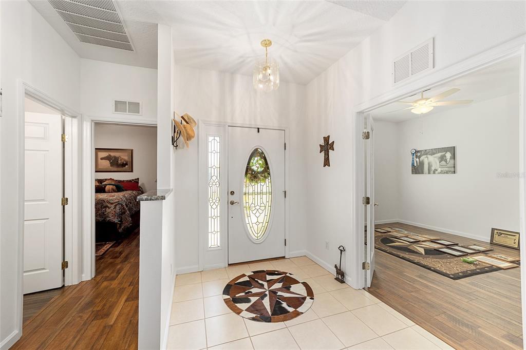 A bright entryway features tile flooring, a white front door, and wood-look laminate flooring nearby — 5751 NW 25TH LOOP, OCALA, FL