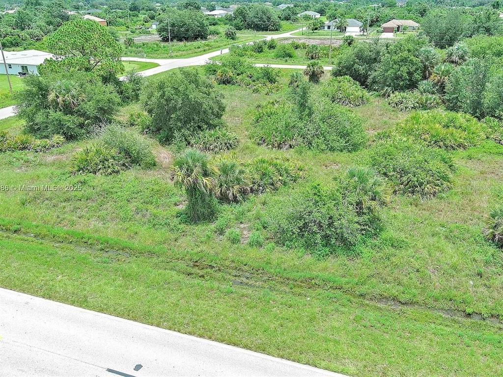 An aerial view shows a vacant, grassy lot with scattered trees and shrubs near a road — 841 MILWAUKEE BOULEVARD, LEHIGH ACRES, FL