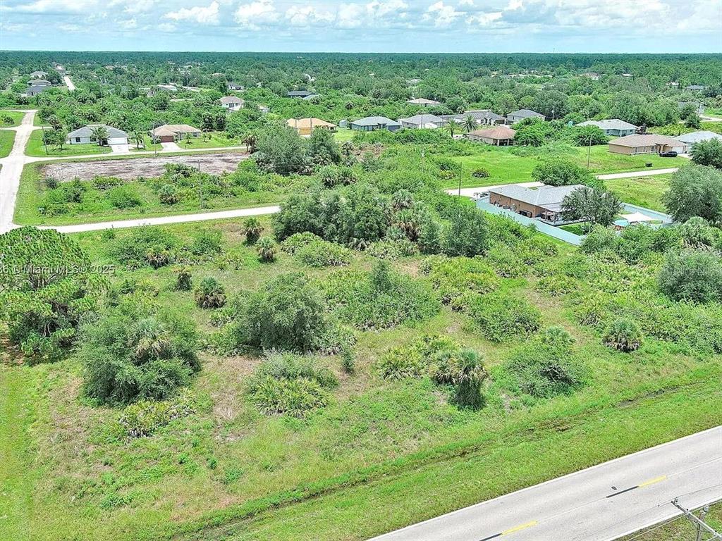 An aerial view shows a vacant, grassy lot surrounded by trees and residential houses — 841 MILWAUKEE BOULEVARD, LEHIGH ACRES, FL