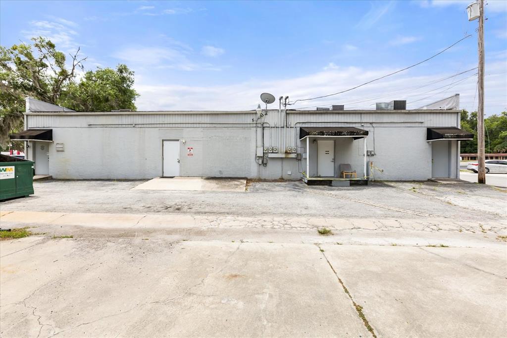 The exterior of a gray commercial building features three doors with awnings and a dumpster — 5053 SE ABSHIER BLVD BOULEVARD, BELLEVIEW, FL