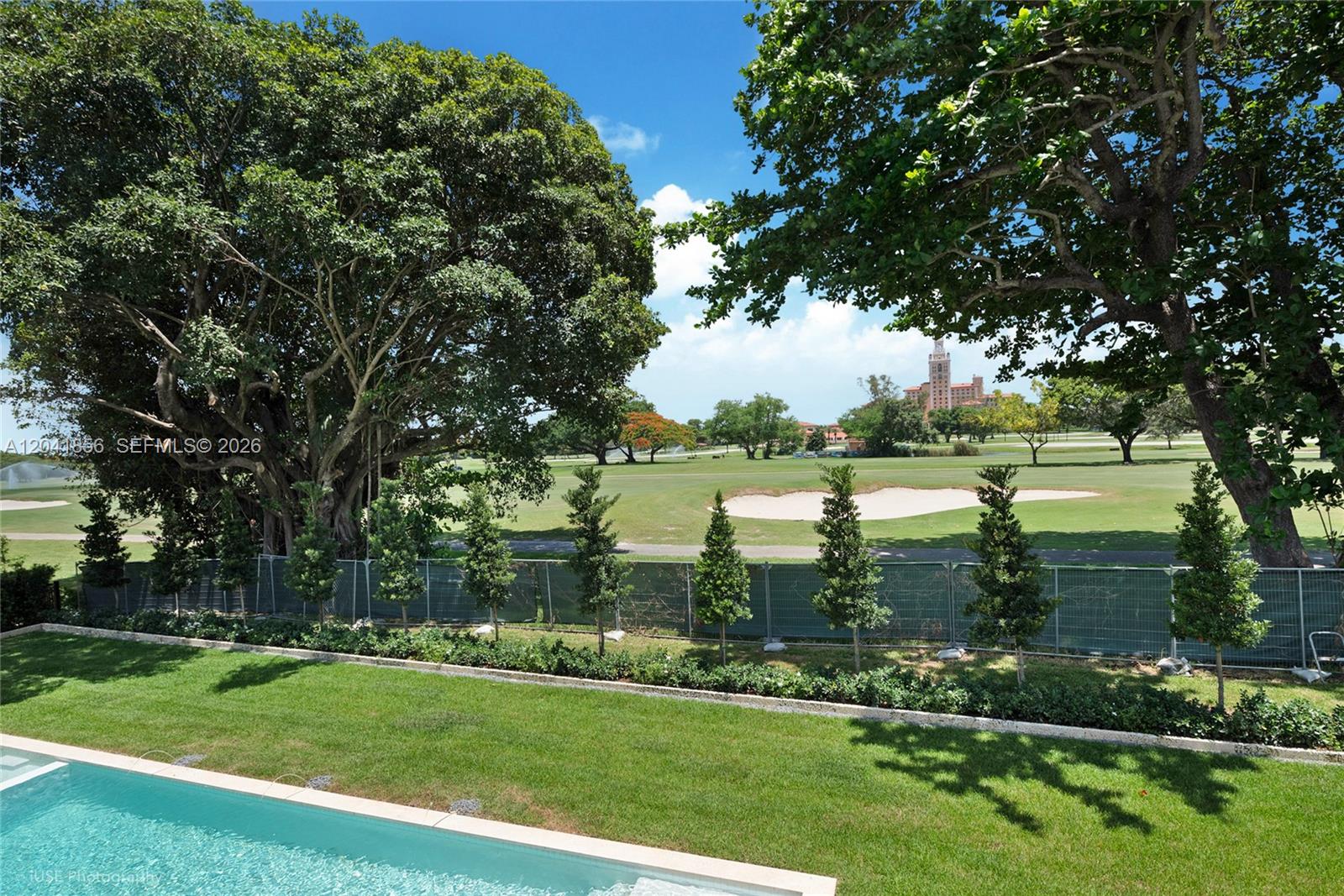 A backyard swimming pool overlooks a green golf course with a large building in distance — 1241 Mariola Ct, Coral Gables FL 33134, CORAL GABLES, FL