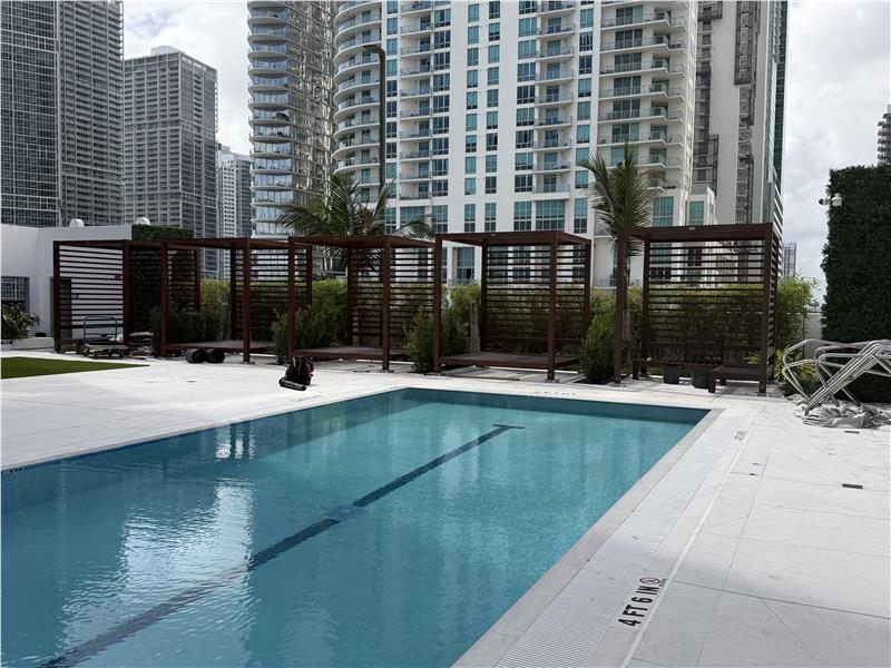 A rectangular swimming pool sits on a patio in front of several wooden cabanas — 335 S Biscayne Boulevard # 4004, Miami FL 33131, MIAMI, FL
