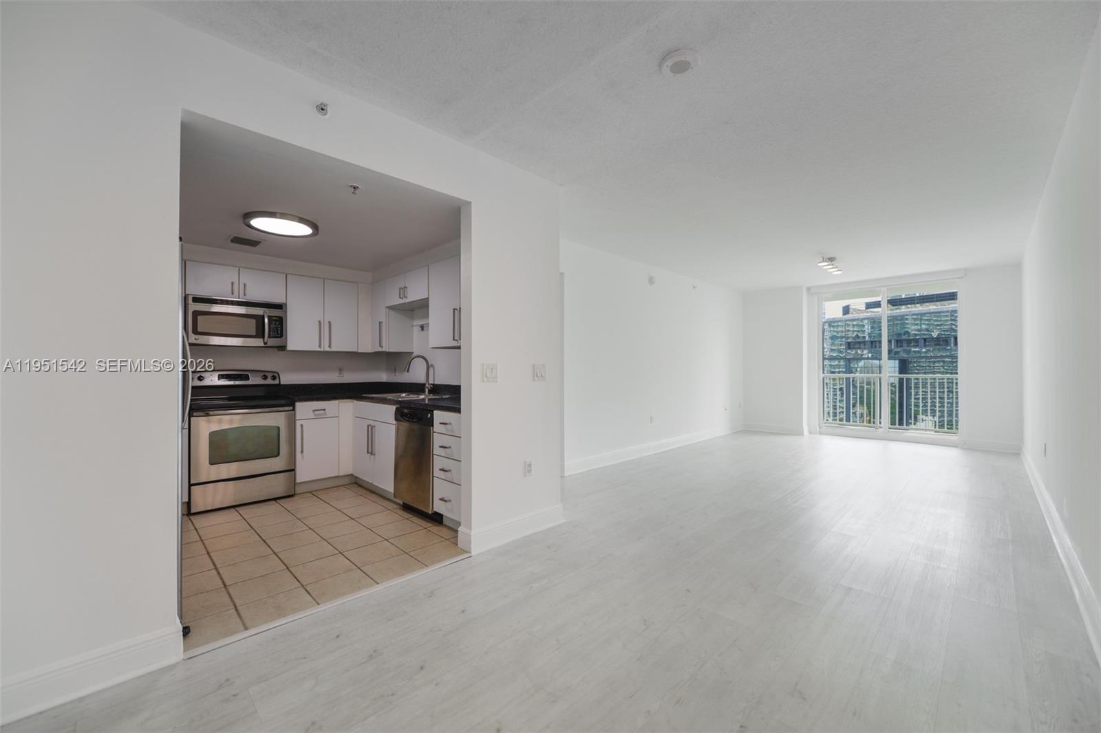 A kitchen with stainless steel appliances and tile flooring opens into a spacious living area — 1250 S Miami Ave # 1906, Miami FL 33130, MIAMI, FL