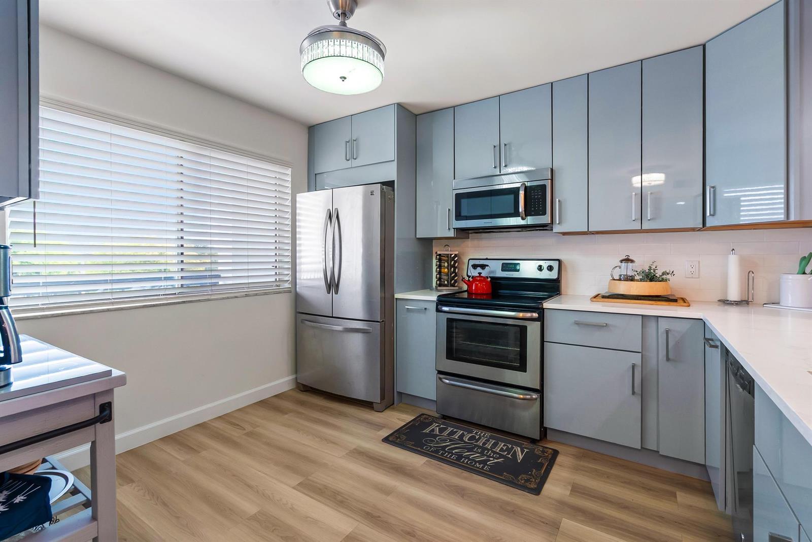 A kitchen features light blue cabinets, stainless steel appliances, and wood-look flooring — 6698 10th Avenue N # 408, FL 33467, FL