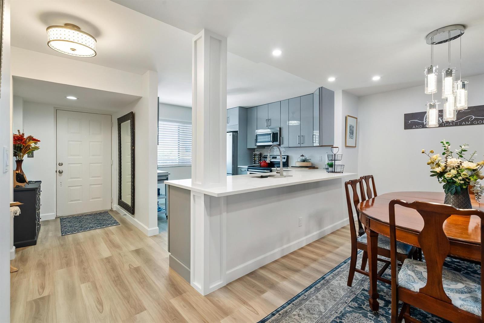 A kitchen with gray cabinets and a white peninsula overlooks a dining area with wood flooring — 6698 10th Avenue N # 408, FL 33467, FL