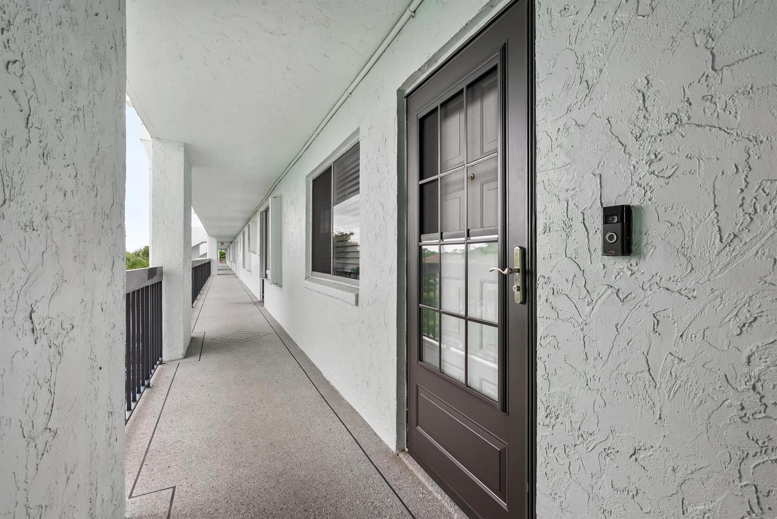 A dark brown door with a glass pane and a doorbell camera on a balcony — 6698 10th Avenue N # 408, FL 33467, FL