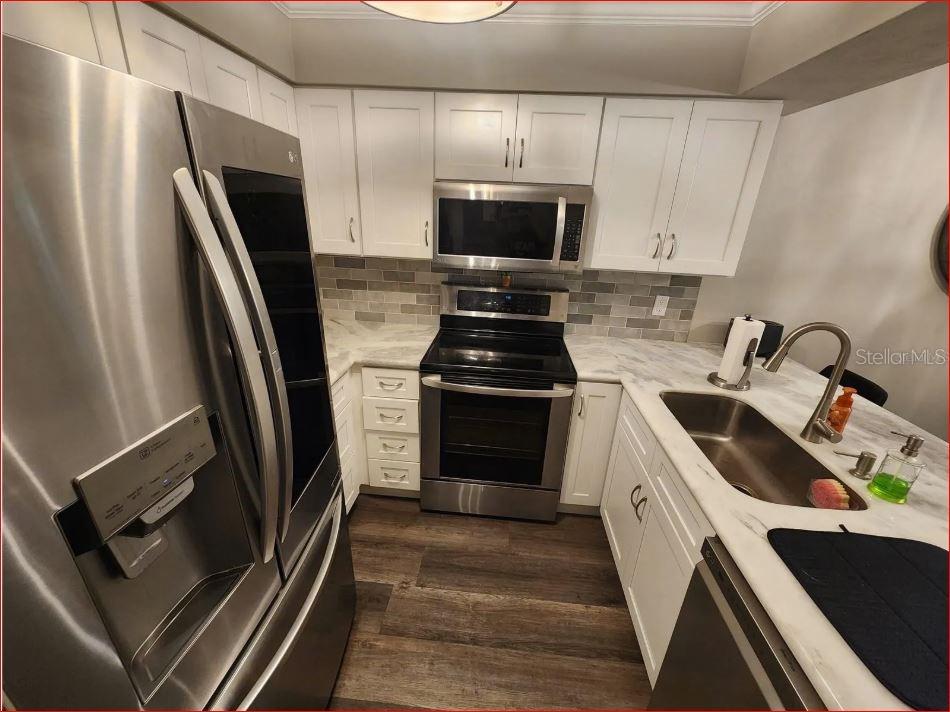 A kitchen with white cabinets, stainless steel appliances, marble-look countertops, and a gray tile backsplash — 2735 SW 35TH PLACE UNIT 804, GAINESVILLE, FL