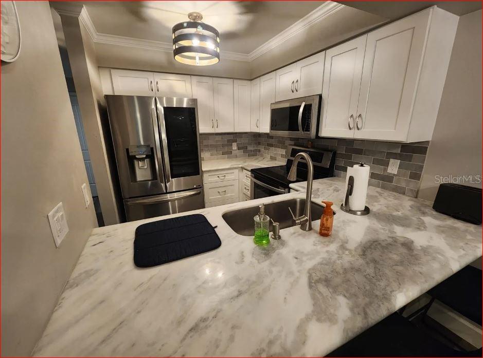 A kitchen features white cabinets, stainless steel appliances, a marble countertop, and a gray backsplash — 2735 SW 35TH PLACE UNIT 804, GAINESVILLE, FL