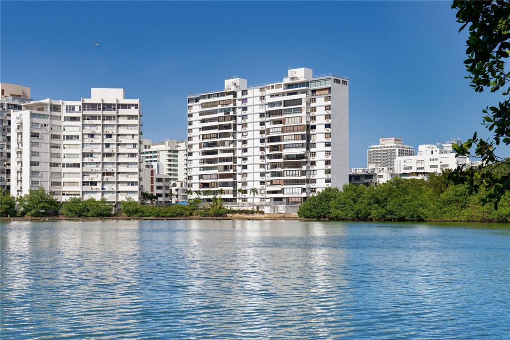 A view of white apartment buildings across a body of water with surrounding trees — 20 DELCASSE STREET UNIT 401, SAN JUAN, PR