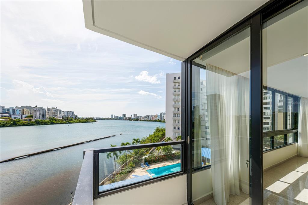 A balcony with a glass railing overlooks a river, a swimming pool, and a city skyline — 20 DELCASSE STREET UNIT 401, SAN JUAN, PR
