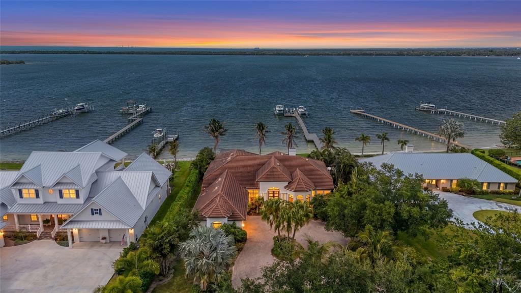 An aerial view shows three waterfront houses with private docks along a large bay at sunset — 7610 DESOTO MEMORIAL HIGHWAY, BRADENTON, FL