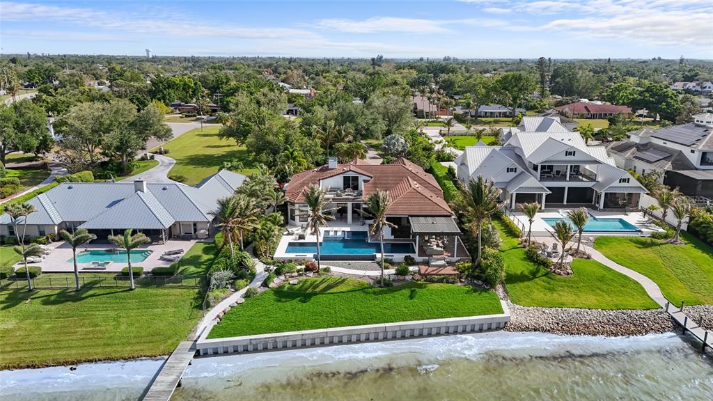 An aerial view shows three waterfront houses with pools and private docks along a shoreline — 7610 DESOTO MEMORIAL HIGHWAY, BRADENTON, FL