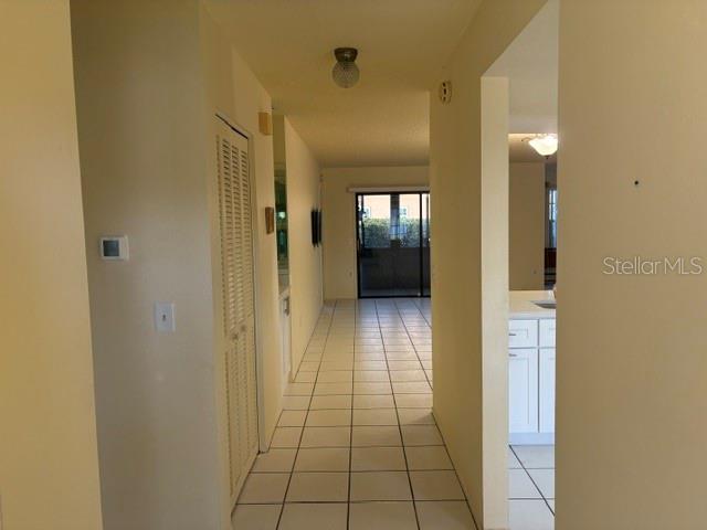 A hallway with white tile flooring leads toward a glass sliding door and a kitchen — 4809 WAKEFIELD COURT, NEW PORT RICHEY, FL